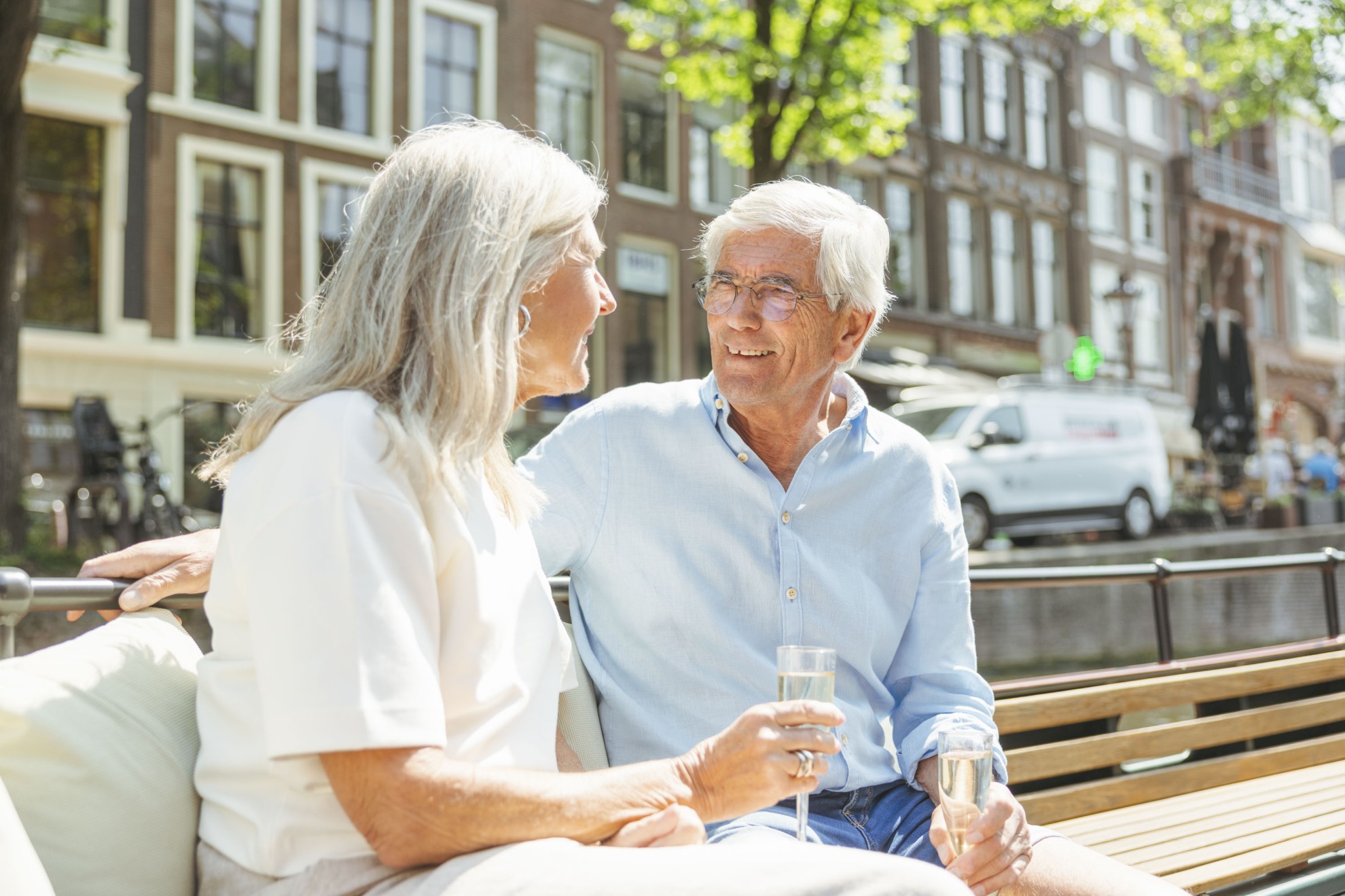 Boaty.nl - Ouder koppel op een boot An elderly couple sits relaxed on a boat in the Amsterdam canals, smiling at each other as they enjoy a glass of wine.