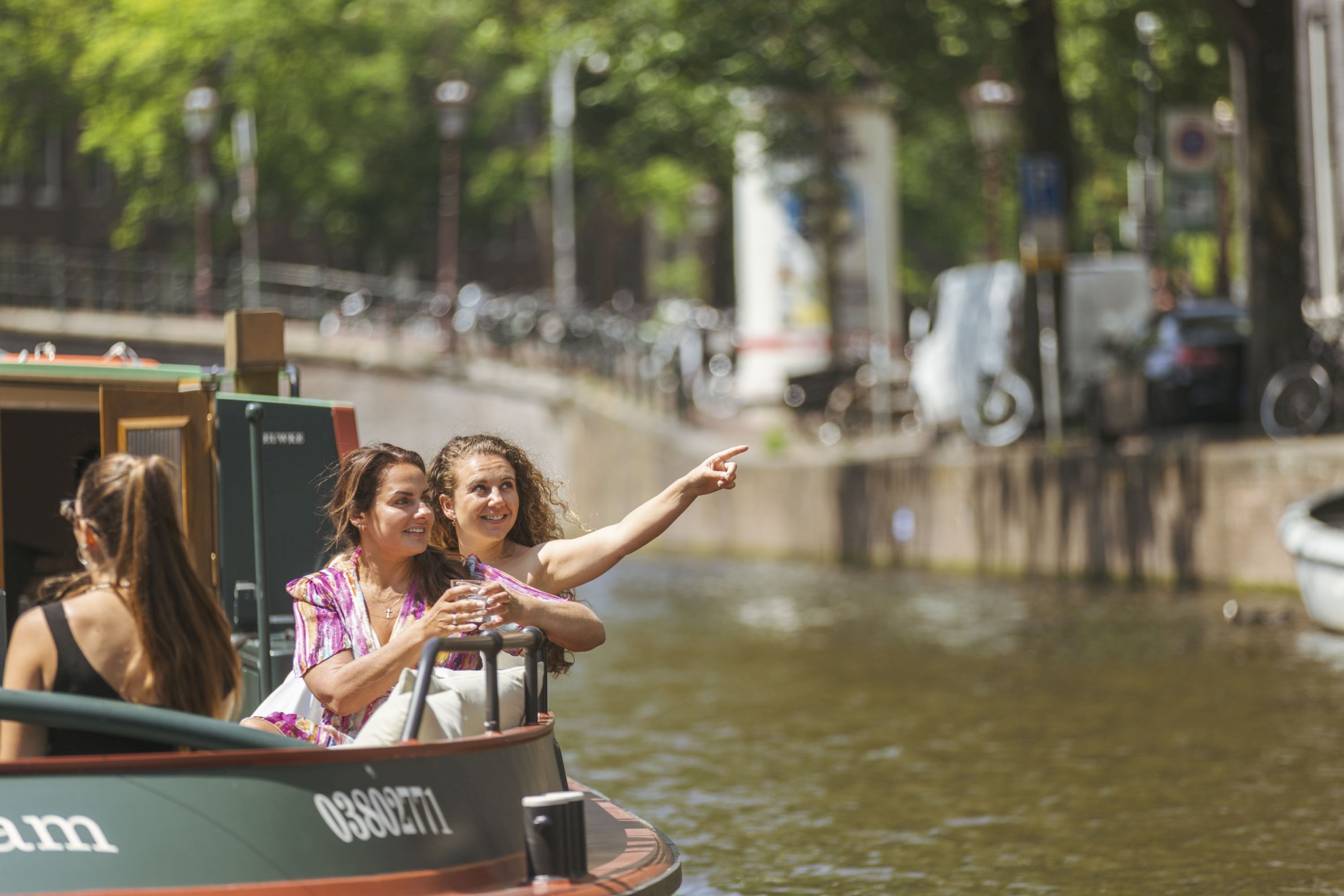 Boaty.nl - Twee vrouwen op een boot Two women enjoy a canal cruise in Amsterdam; one of them points enthusiastically at something in the distance.