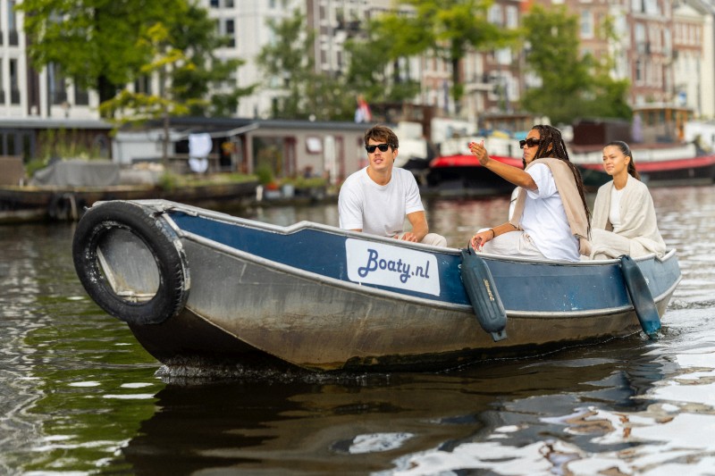 Three friends are sailing through an Amsterdam canal in a small rental boat while enjoying the view of the city.